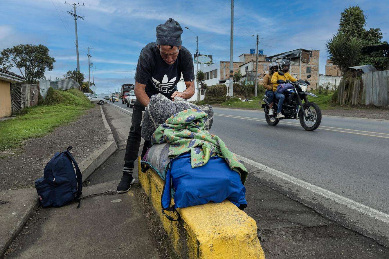 A migrant waits by the side of the road with his belongings in Colombia