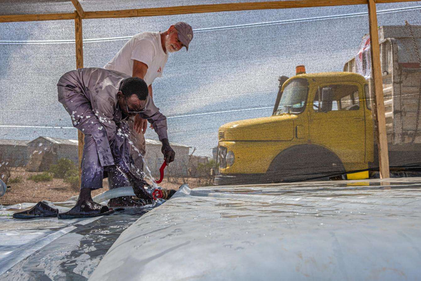 Two MSF team members work on water infrastructure with a yellow truck in the background in Chad.
