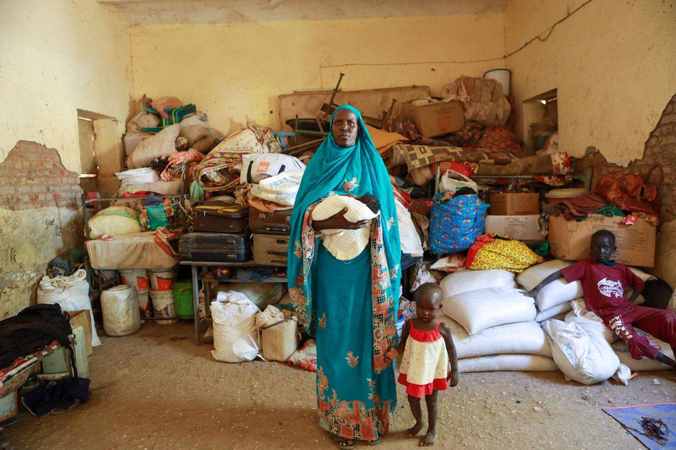 A displaced woman and child stand in a room full of luggage in Sudan.