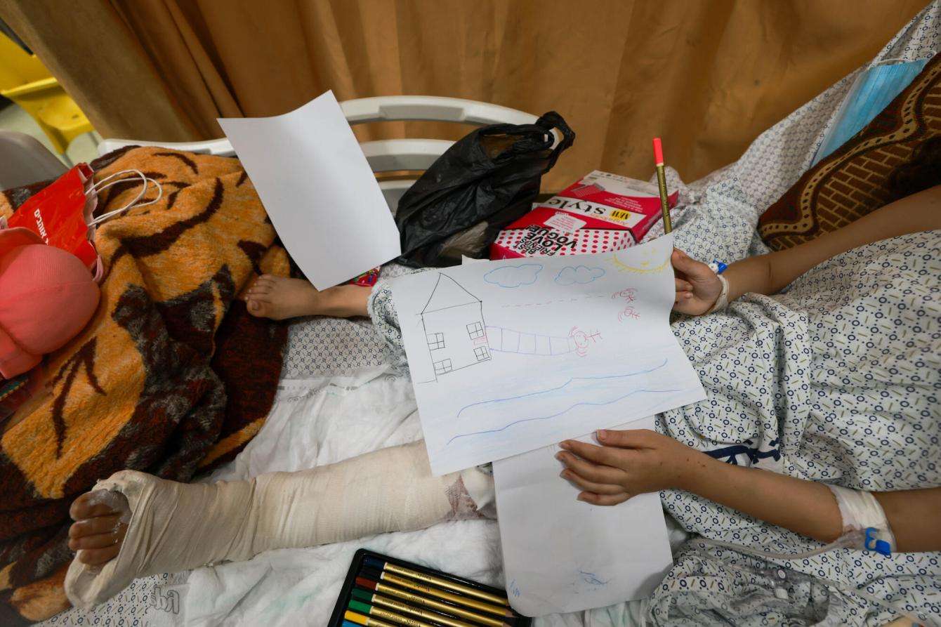 A child patient lies on a hospital bed in a cast and with a drawing on her lap in Gaza.