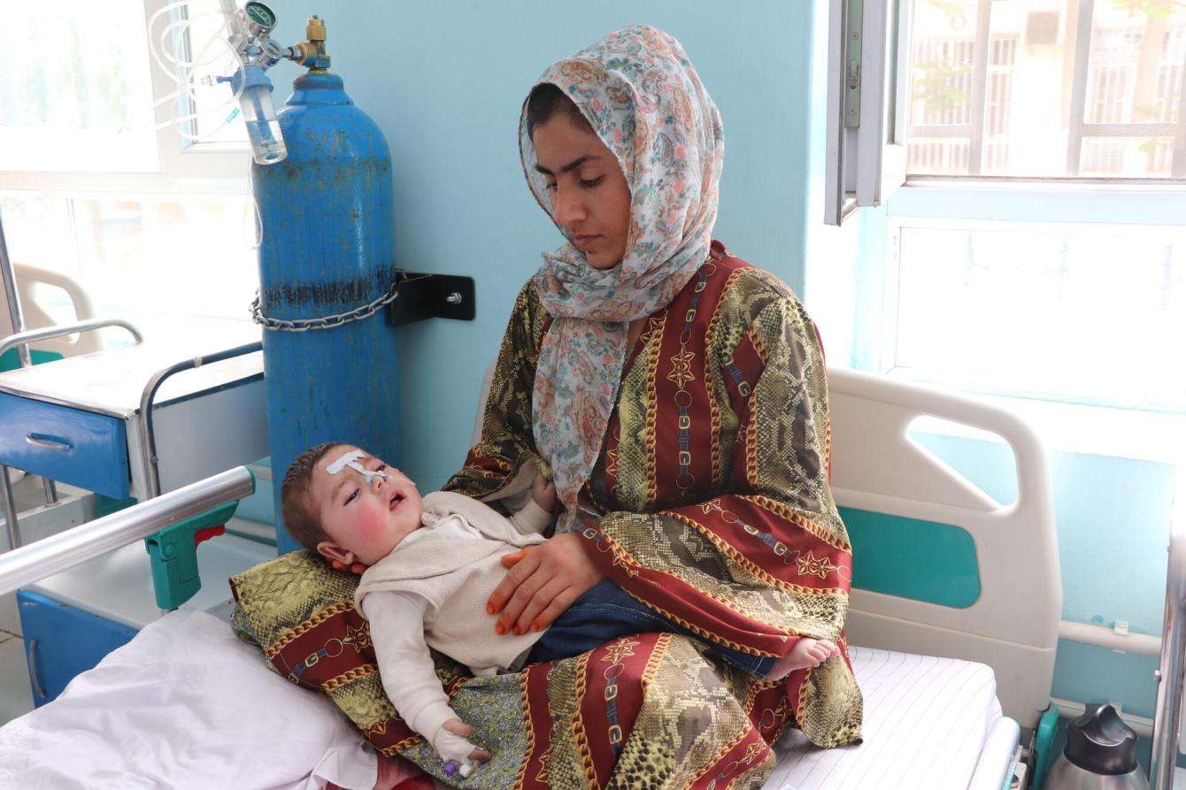 A mother holds her sick child with measles symptoms on a hospital bed in Afghanistan.