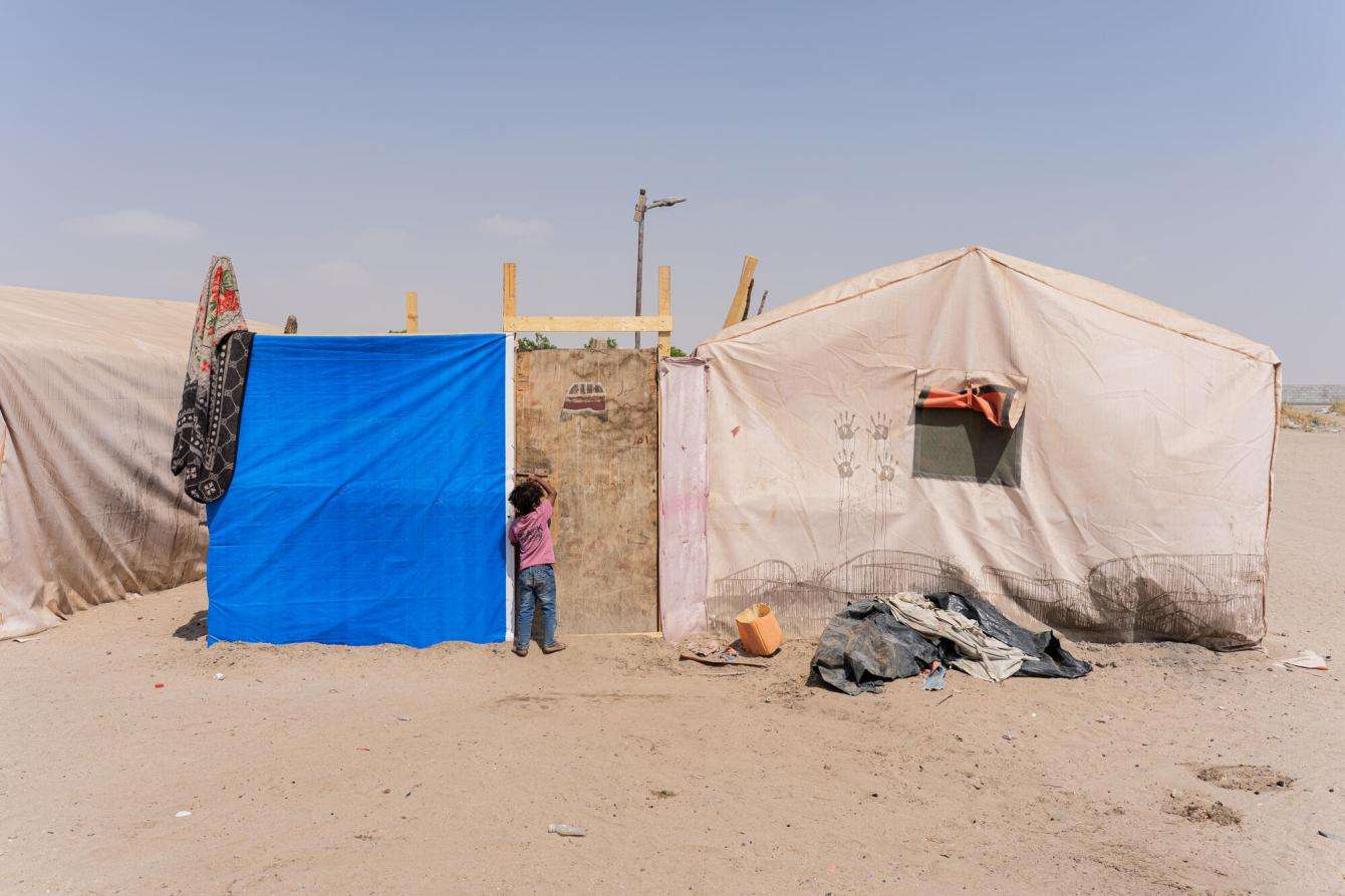 A little girl knocks on the door of her tent at the entrance of Atira camp, Lahj governorate, Yemen.