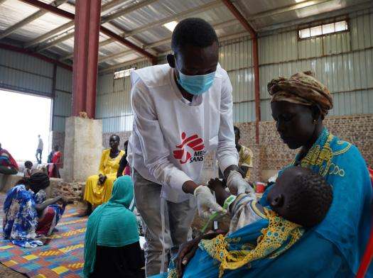 MSF medical staff in white vest treats a Sudanese refugee mother with child in South Sudan.