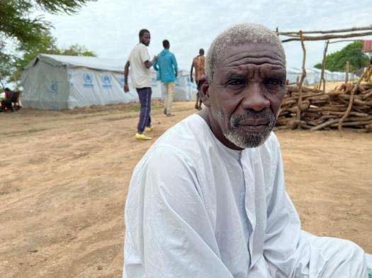 Sudanese man wearing white sits on ground outside refugee camp in Central African Republic