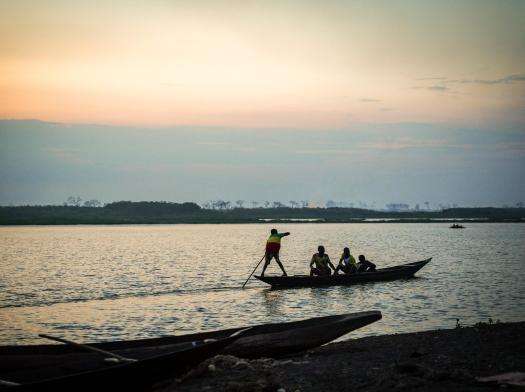 Silhouette of young boy rowing canoe across floodwater during sunset in South Sudan