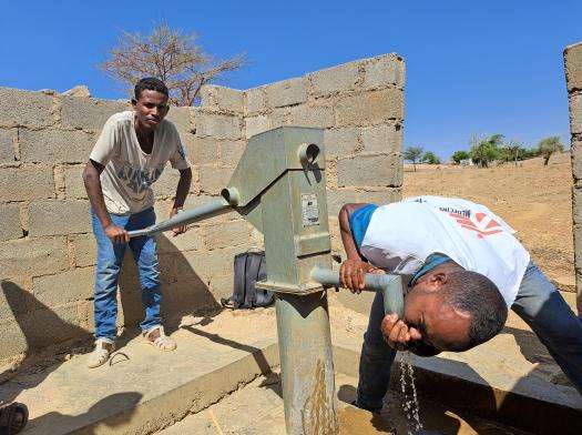 Two MSF water and sanitation experts drink water from a hand pump in  May Kwait, a village in Tigray, Ethiopia, 