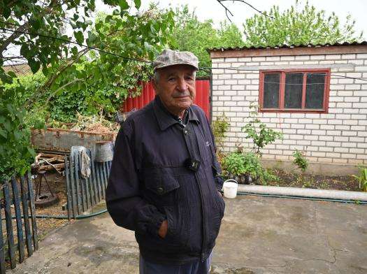 Elderly man in dark jacket standing in front of a white building in Ukraine