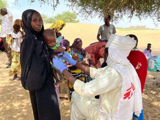 A woman holds a child who is being examined by a doctor. 