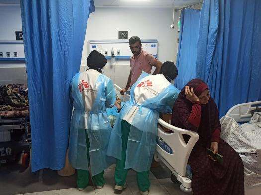 MSF teams treat a patient at al Shifa Hospital while a woman sits in the next bed.