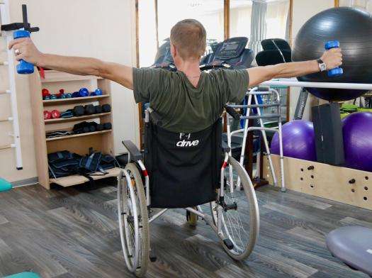 A patient in a wheelchair holds weights on each arm as part of his physiotherapy exercises.