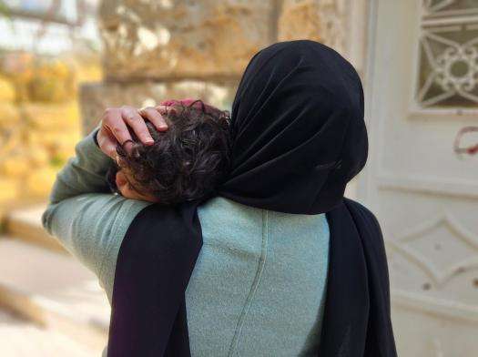 The back of a Palestinian woman holding her child.