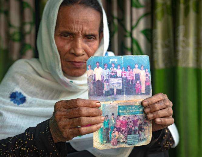 An older woman holds up two photographs of her family members.