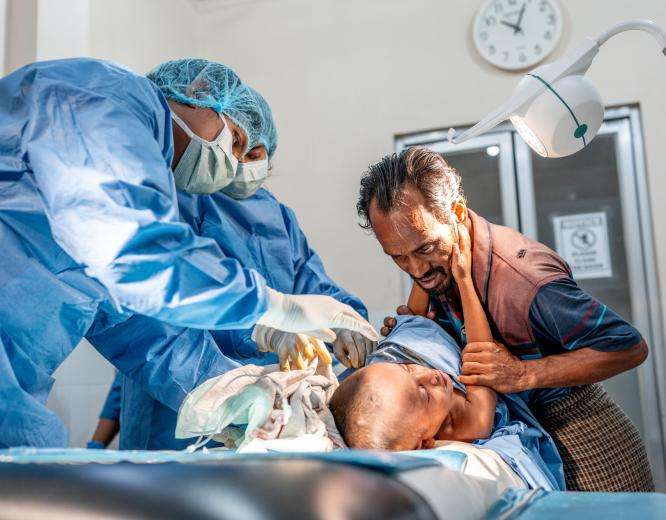 Anis Mohammad tries to comfort his 4-year-old son, Shofi, as he receives treatment for multiple abscesses in the emergency room at MSF's Kutupalong Hospital. 