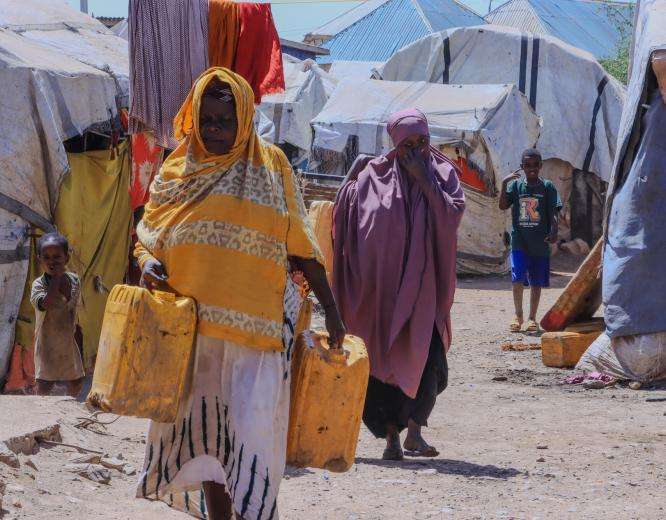 Women carry empty jerrycans through Bur Shebelow displacement camp, Baidoa, Somalia, to collect water from a distribution point.