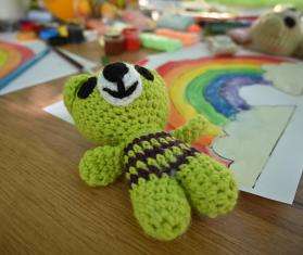 green knit toy lays on wooden table with drawing of a rainbow