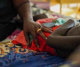 A woman lays her hand on a child lying in a pediatric ward with measles at MSF's facility in Bentiu camp, South Sudan.
