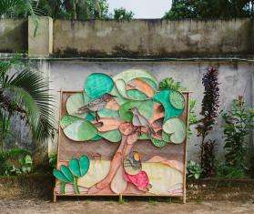 A 3D mural made of many shades of green featuring a banyan tree in the center, a bird, and a woman.