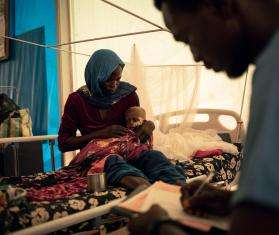 A woman holds her infant son on her lap in a hospital bed in Chad. 