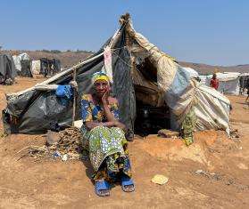 A woman sitting in front of a tent looks at camera in Burundi. 