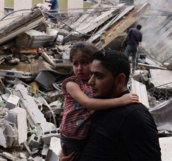 A man holding a child with wreckage from Israeli bombardment in Gaza behind them.