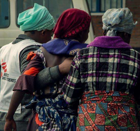 An MSF staff member and two other women link arms in DR Congo.